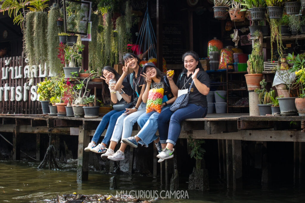 Four happy young women sitting on the canal side of a shop in Bangkok. Happy and smiling and doing the peace sign