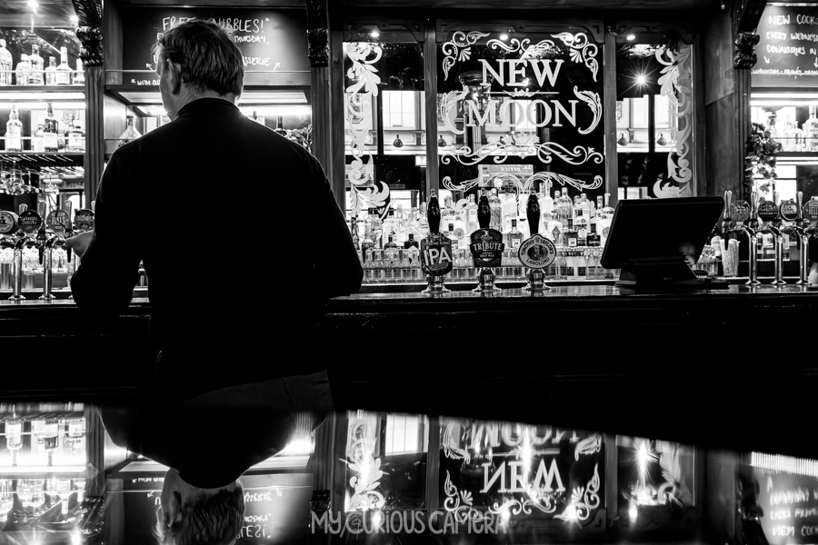 New Moon pub inside James ordering a pint at the bar there is a reflection on the table