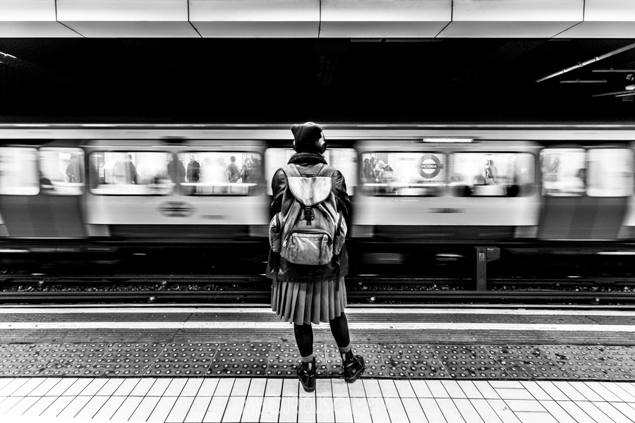 Girl standing at London tube station with train wooshing by in a blur