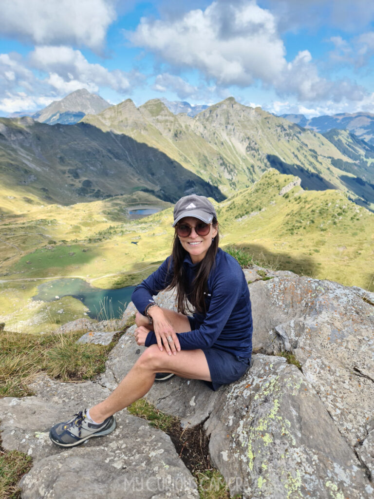 Nina solo adventure travelling in France. Here she sits smiling on the top of a mountain
