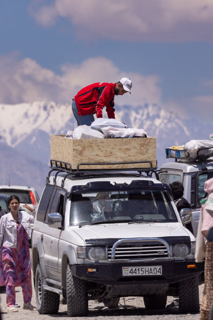 An overland 4x4 expedition vehicle being stacked high with heavy cargo bags during a cross-border market day between Tajikistan and Afghanistan.